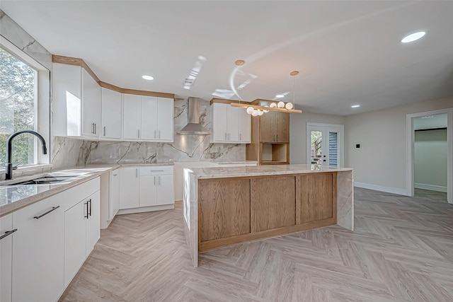 kitchen featuring sink, a center island, white cabinetry, and wall chimney range hood