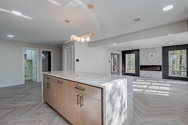 kitchen with a center island, light brown cabinets, light stone countertops, a premium fireplace, and light parquet flooring