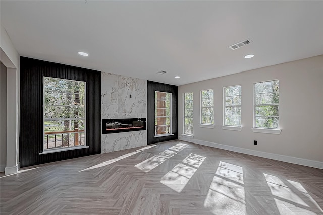 unfurnished living room with light parquet flooring, a large fireplace, and a healthy amount of sunlight