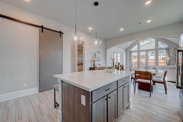 kitchen with ceiling fan, hanging light fixtures, a barn door, vaulted ceiling, and a kitchen island