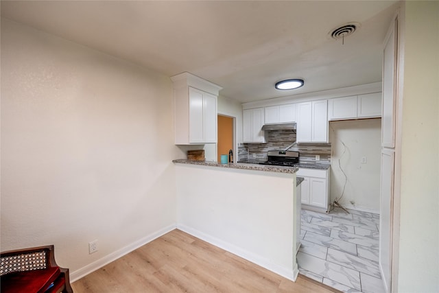 kitchen featuring light stone countertops, backsplash, light hardwood / wood-style flooring, stainless steel stove, and white cabinetry