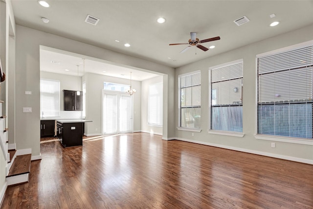 unfurnished living room with dark hardwood / wood-style floors, ceiling fan with notable chandelier, and a wealth of natural light