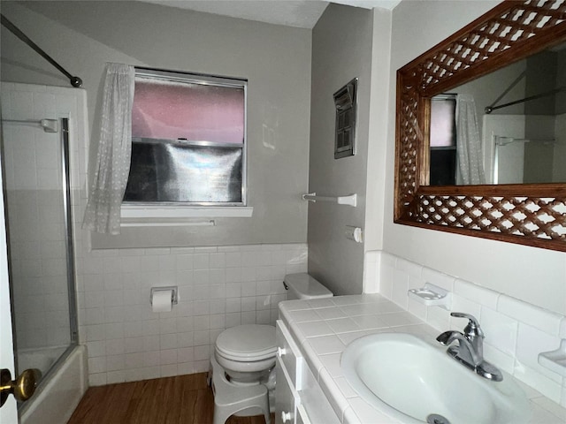 full bathroom with bath / shower combo with glass door, vanity, tile walls, hardwood / wood-style floors, and toilet