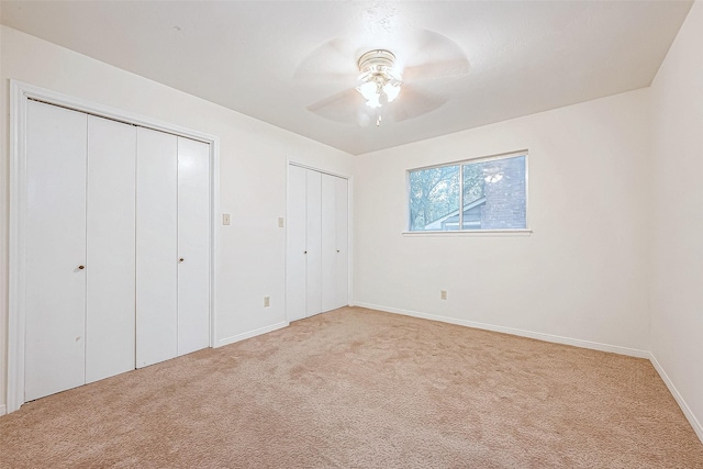 unfurnished bedroom featuring multiple closets, ceiling fan, and light carpet