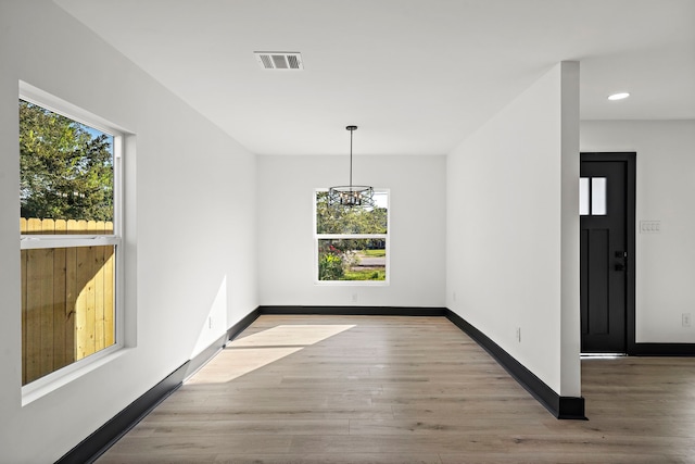 unfurnished dining area featuring light hardwood / wood-style floors, a wealth of natural light, and an inviting chandelier