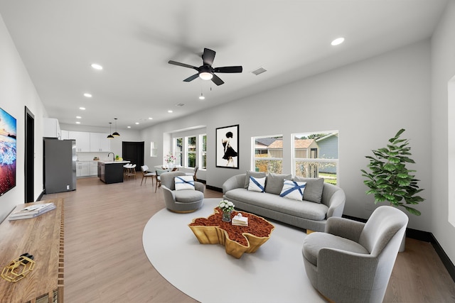 living room featuring ceiling fan, light wood-type flooring, and sink