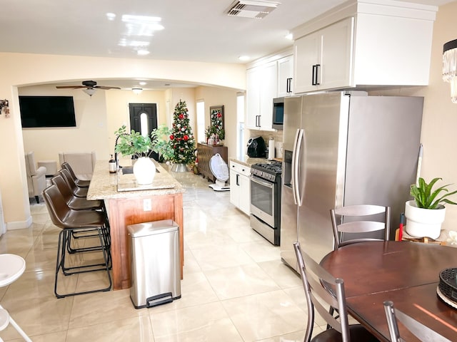 kitchen featuring light stone countertops, appliances with stainless steel finishes, ceiling fan, white cabinets, and a center island