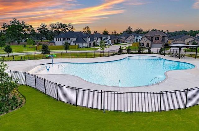 pool at dusk featuring a community pool, a residential view, fence, and a lawn