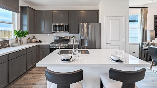 kitchen with a breakfast bar, stainless steel appliances, light countertops, backsplash, and a sink