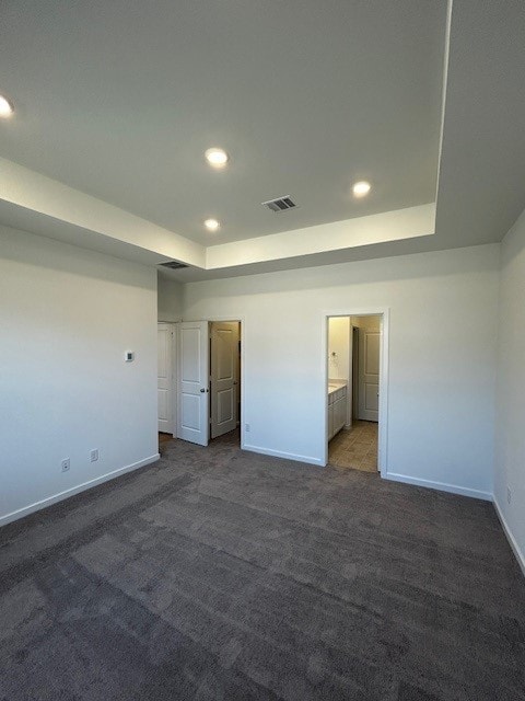 unfurnished bedroom featuring carpet floors, a tray ceiling, and baseboards