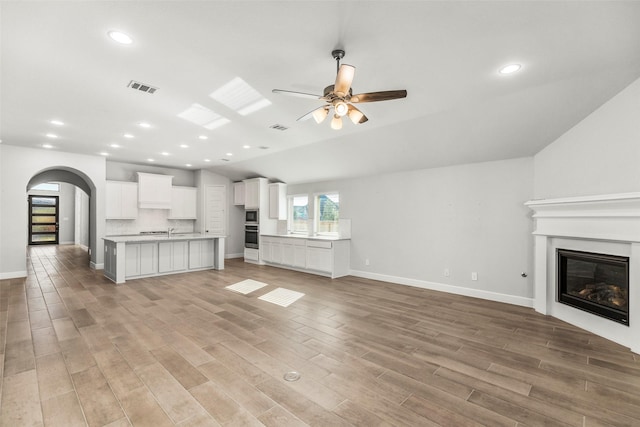 unfurnished living room featuring vaulted ceiling, light hardwood / wood-style flooring, ceiling fan, and sink