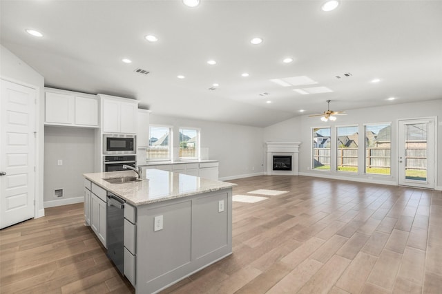 kitchen with lofted ceiling, light wood-type flooring, an island with sink, white cabinetry, and stainless steel appliances