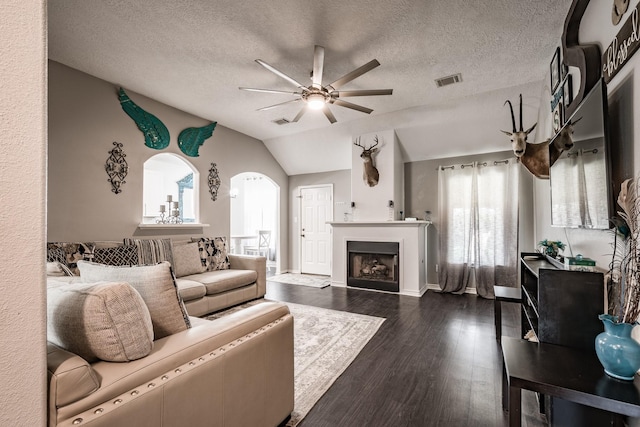 living room with a textured ceiling, ceiling fan, dark wood-type flooring, and vaulted ceiling