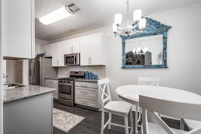 kitchen with appliances with stainless steel finishes, dark wood-type flooring, sink, a notable chandelier, and white cabinets