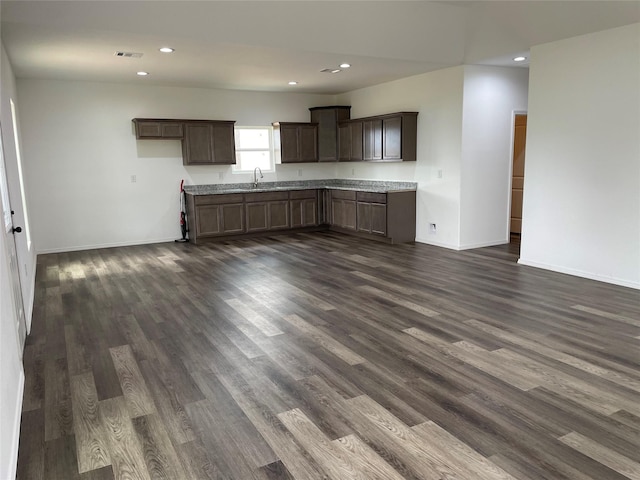 kitchen with light stone countertops, dark brown cabinets, dark wood-type flooring, and sink