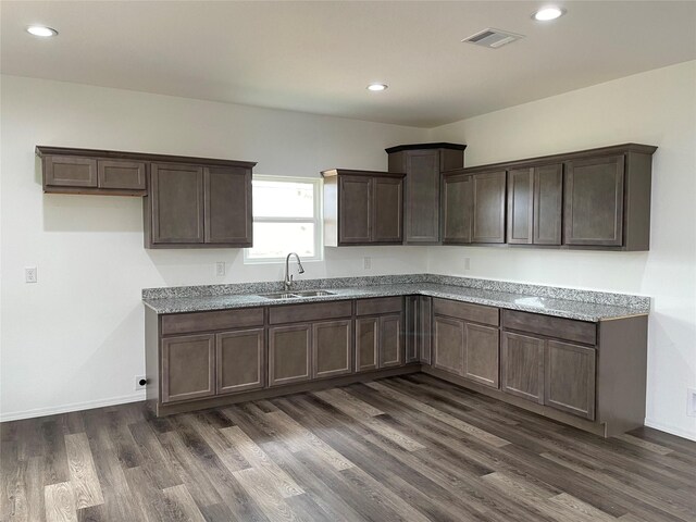 kitchen with dark hardwood / wood-style flooring, light stone counters, dark brown cabinetry, and sink