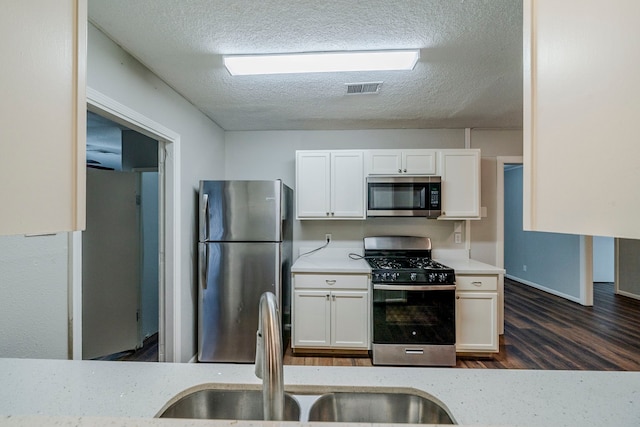 kitchen with dark wood-type flooring, white cabinets, sink, a textured ceiling, and appliances with stainless steel finishes