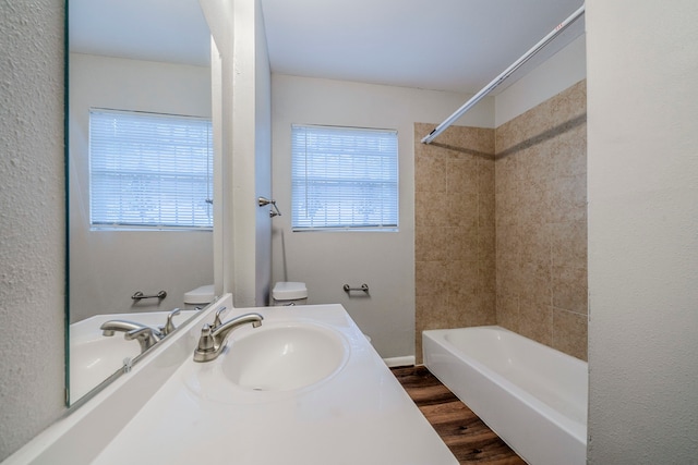 full bathroom with sink, hardwood / wood-style floors, tiled shower / bath combo, and toilet