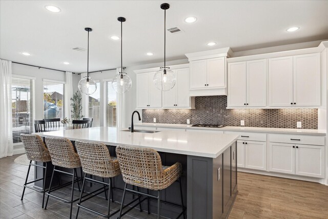 kitchen with a kitchen island with sink, sink, white cabinets, and wood-type flooring