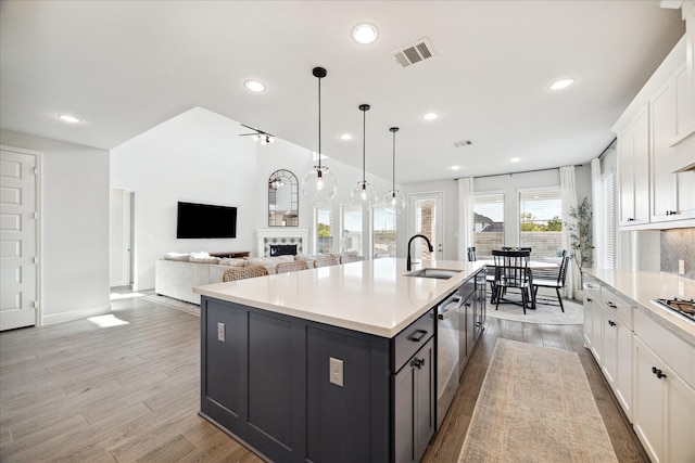 kitchen with a kitchen island with sink, white cabinets, sink, light hardwood / wood-style flooring, and decorative light fixtures