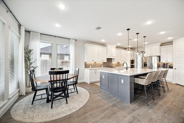 kitchen with a spacious island, sink, stainless steel refrigerator with ice dispenser, light wood-type flooring, and white cabinetry