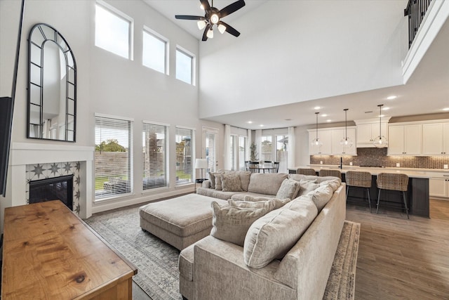 living room featuring a tile fireplace, sink, hardwood / wood-style flooring, ceiling fan, and a towering ceiling