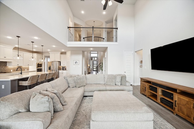 living room with ceiling fan, sink, a towering ceiling, and hardwood / wood-style flooring