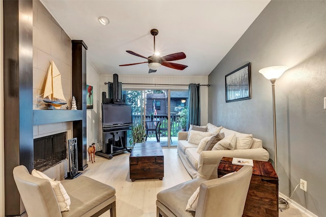 living room with a large fireplace, light hardwood / wood-style floors, vaulted ceiling, and ceiling fan