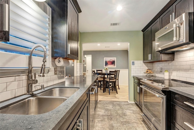 kitchen featuring dark brown cabinetry, sink, stainless steel appliances, backsplash, and dark stone counters