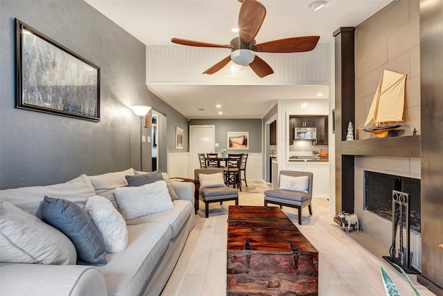 living room with a tiled fireplace, ceiling fan, and light hardwood / wood-style floors