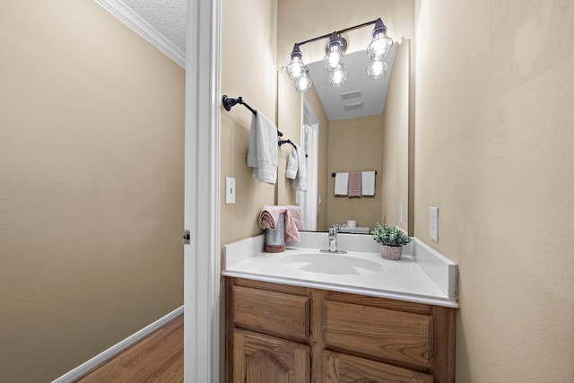 bathroom featuring vanity, wood-type flooring, ornamental molding, and a textured ceiling