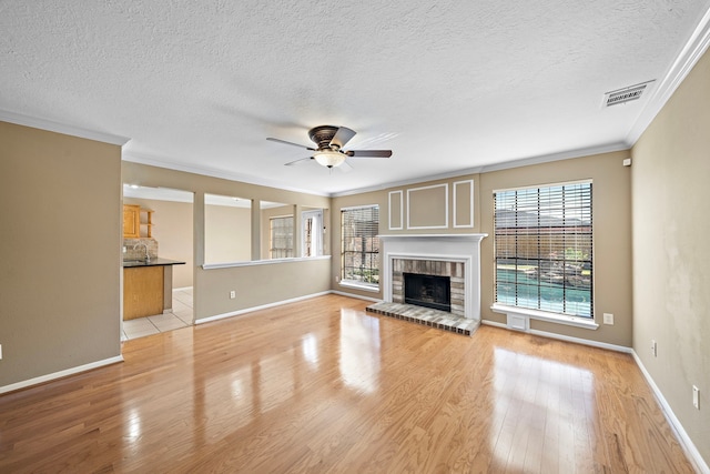 unfurnished living room featuring ornamental molding, a textured ceiling, ceiling fan, a fireplace, and light hardwood / wood-style floors