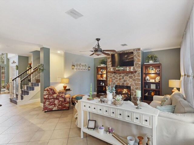 tiled living room with ceiling fan, a stone fireplace, and ornamental molding