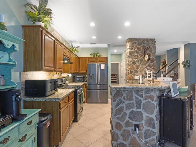 kitchen with decorative backsplash, light tile patterned floors, an island with sink, appliances with stainless steel finishes, and light stone counters