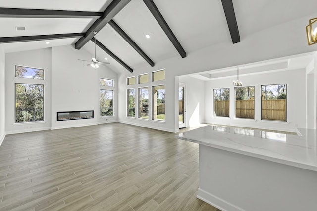 unfurnished living room with beamed ceiling, ceiling fan with notable chandelier, light hardwood / wood-style flooring, and plenty of natural light