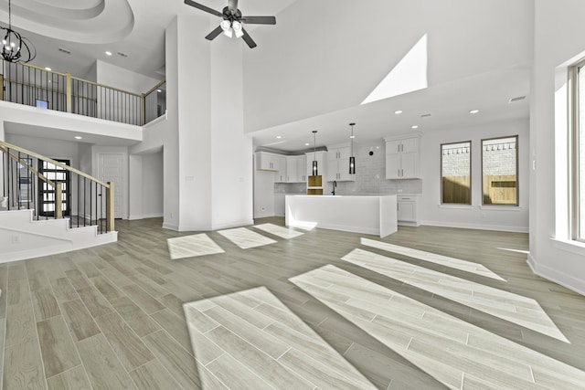 unfurnished living room featuring ceiling fan with notable chandelier, a high ceiling, and light hardwood / wood-style flooring