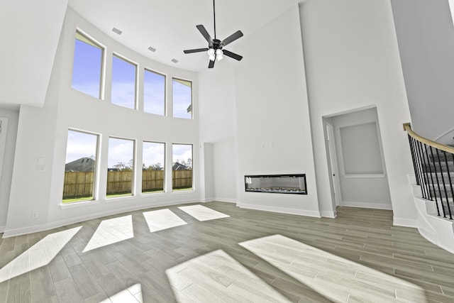 unfurnished living room featuring wood-type flooring, a towering ceiling, and a healthy amount of sunlight