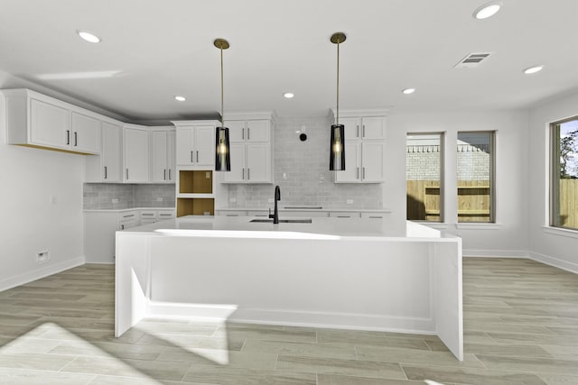 kitchen featuring white cabinets, decorative light fixtures, sink, and an island with sink