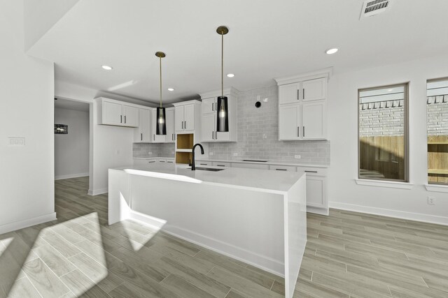 kitchen with white cabinetry, sink, hanging light fixtures, an island with sink, and light wood-type flooring