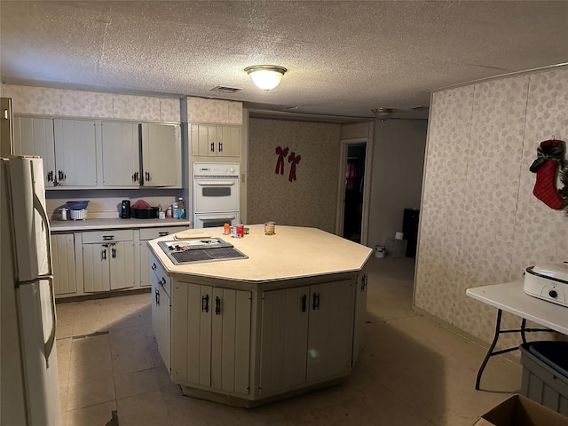 kitchen featuring a textured ceiling, white appliances, white cabinetry, and a kitchen island