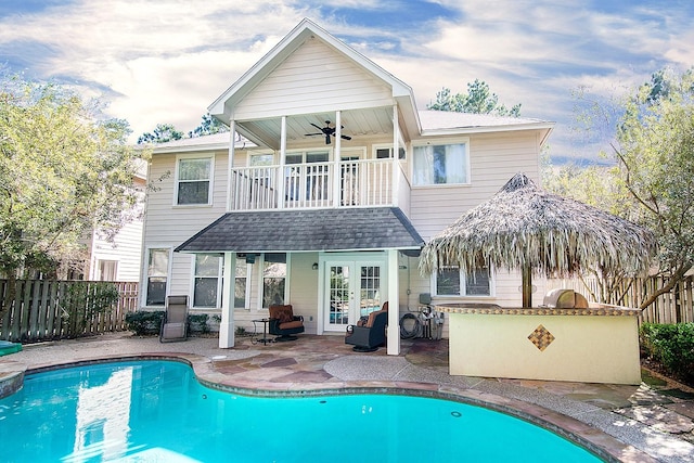 rear view of property featuring a fenced in pool, french doors, ceiling fan, a balcony, and a patio