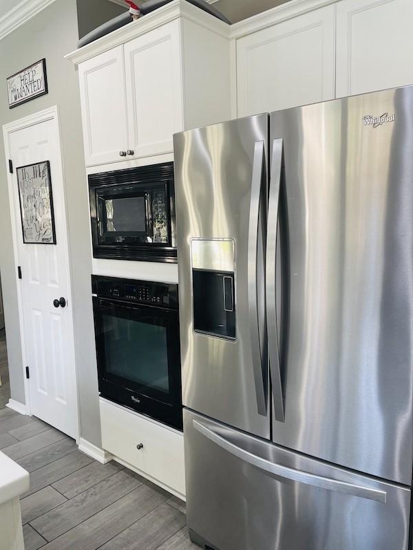 kitchen featuring white cabinets, dark hardwood / wood-style flooring, ornamental molding, and black appliances