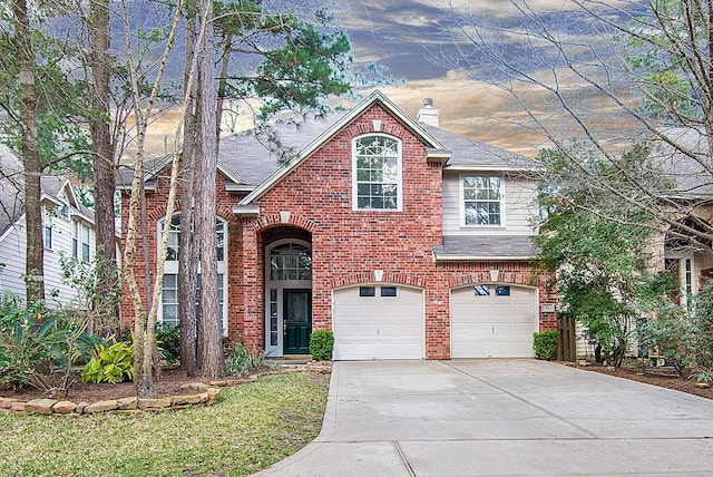 traditional-style house featuring concrete driveway, a garage, brick siding, and a chimney