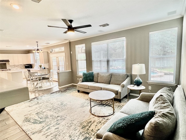 living room with ceiling fan with notable chandelier, light hardwood / wood-style floors, crown molding, and a wealth of natural light