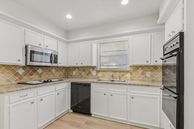 kitchen with white cabinetry, sink, light stone counters, light hardwood / wood-style floors, and black appliances