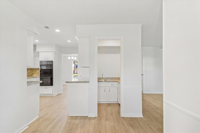 kitchen with white cabinetry, black double oven, light stone countertops, and light wood-type flooring