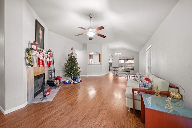 living room featuring a fireplace, ceiling fan with notable chandelier, wood-type flooring, and lofted ceiling