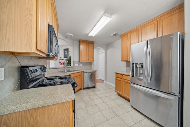 kitchen featuring decorative backsplash, light stone counters, stainless steel appliances, sink, and light tile patterned flooring