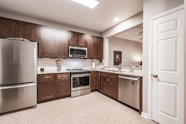 kitchen with sink, tasteful backsplash, light stone counters, dark brown cabinetry, and stainless steel appliances