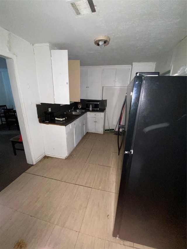 kitchen featuring white cabinets, sink, black fridge, and a textured ceiling